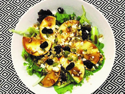 fresh salad featuring slices of pazazz apples all on a white plate on a mosaic black and white patterned table cloth.