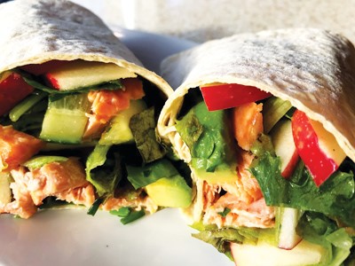 salmon, greens, and Pazazz apples slices encompassed in flour wraps on a white plate.
