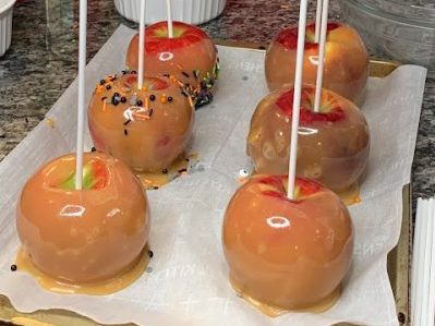 Caramel apples sitting on parchment paper on a baking sheet on a crowded kitchen counter