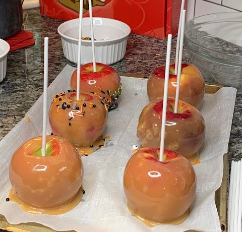 Caramel apples sitting on parchment paper on a baking sheet on a crowded kitchen counter