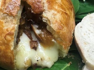 baked brie spilling out of the interior of a baked loaf of bread. This all sits atop a bed of greens.